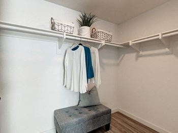 A white chair with a grey cushion is in front of a white wall with a coat hanging on a rail.